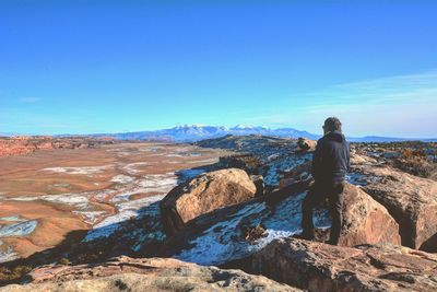 Rear view of man on rock against blue sky