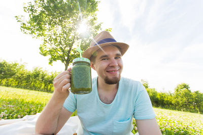 Portrait of smiling young man drinking against plants