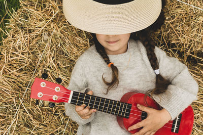 Cute girl wearing hat holding guitar lying on grass outdoors