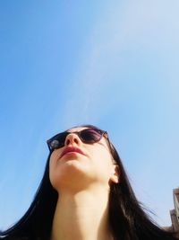 Low angle portrait of young woman against clear blue sky