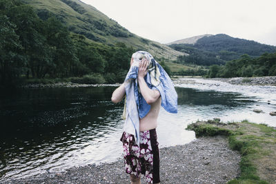 Shirtless man standing by lake with towel