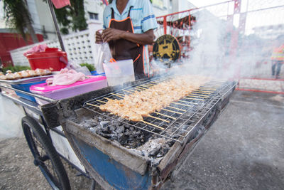 Midsection of male vendor cooking meat on barbecue in city