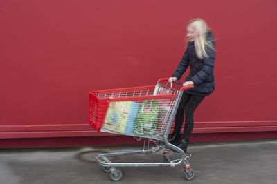 Playful girl on shopping cart against wall