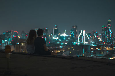 Rear view of woman looking at illuminated cityscape against sky