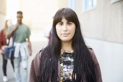 Portrait of young woman with long hair standing at university campus with friends in background