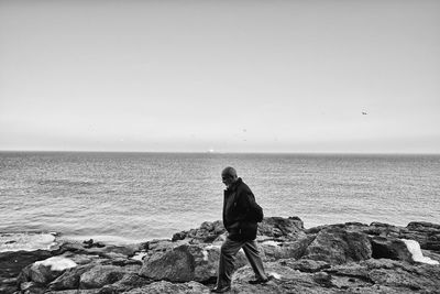 Side view of man walking on rocks by sea against clear sky