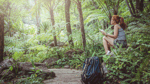 Low angle view of woman holding book sitting on rock in forest