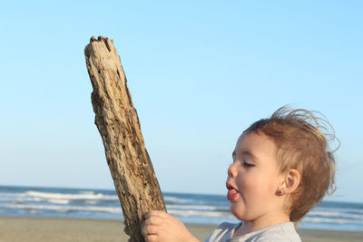 Close-up of boy on tree trunk against clear sky