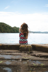 Rear view of woman sitting on retaining wall against sky