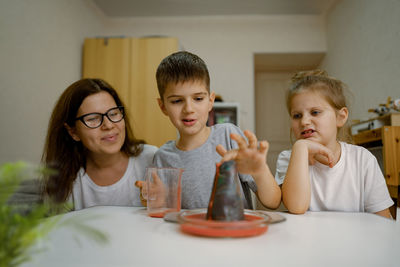 Mom and children at home are conducting an experiment with volcanic eruption.