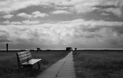 Side view of empty bench on landscape against clouds