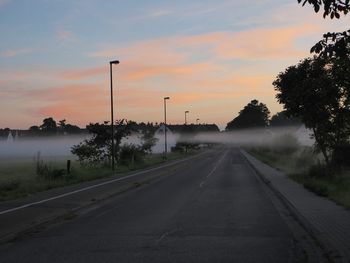 Road by trees against sky during sunset