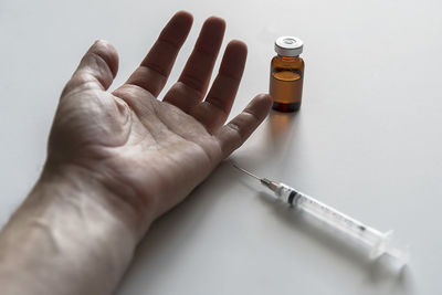 Cropped hand of man by syringe and vial on white table