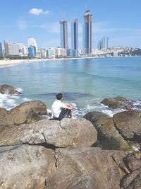 Man sitting on rock by sea against sky