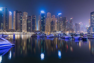 Boats moored in illuminated buildings against sky at night