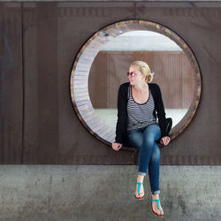 Full length of woman sitting by wall outdoors