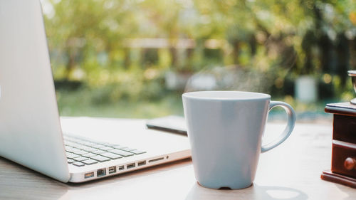 Close up cup of coffee, coffee with smoke on desk table with laptop computer background in morning.