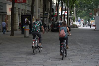 Rear view of man and woman riding bicycle at city street