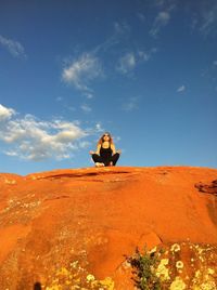Woman sitting on rock formation against sky