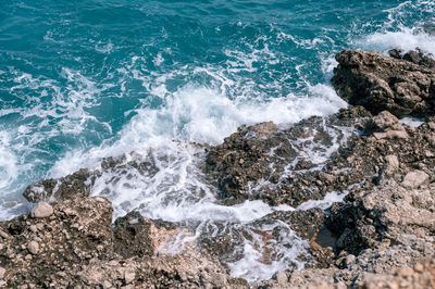 Foamy waves of clear blue sea water beat against the rocky shore of the ocean