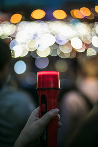 Cropped hand of protestor holding flashlight against illuminated light at night