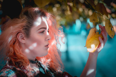 Close-up of thoughtful young woman with dyed hair touching autumn leaf