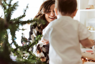 Mother playing with baby by christmas tree at home