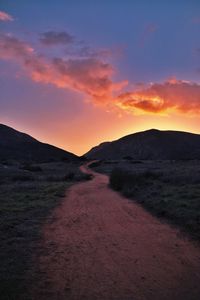 Dirt road amidst mountains against sky during sunset