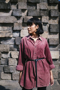 Woman looking away while standing against wall