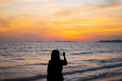 Silhouette person standing by sea against sky during sunset