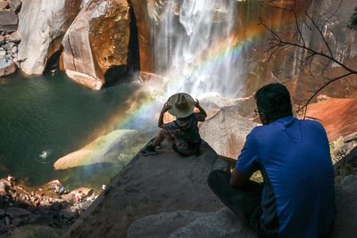 Rear view of men on rock against waterfall