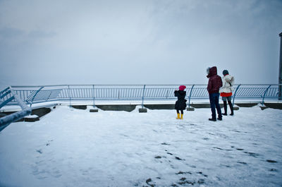 People standing on snow covered shore against sky