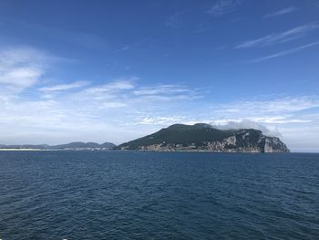 Scenic view of sea by mountain against sky