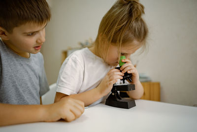 Children, girl and boy at home in the room look through microscope