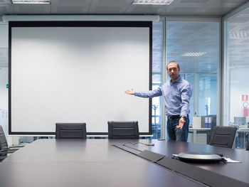 Businessman pointing towards projection screen while standing in board room at office