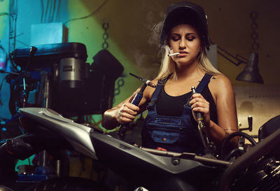 Woman repairing motorcycle while smoking at workshop