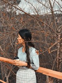 Low section of woman holding smart phone while standing on tree