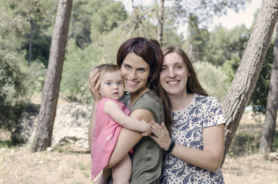 Portrait of happy friends against tree trunk