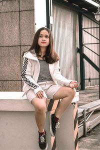 Full length of young woman sitting on retaining wall