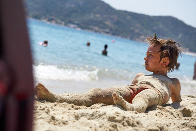 Boy covered with sand lying at beach