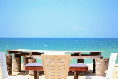 Chairs and table by sea against blue sky