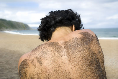 Rear view of shirtless man with sand on back at beach