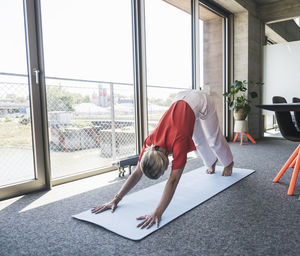 Businesswoman practicing adho mukha svanasana on exercise mat in office