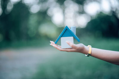 Cropped hand of woman holding model home in park