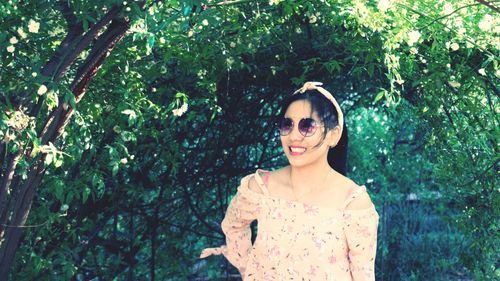 Smiling young woman standing by tree at park