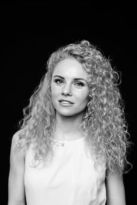 Portrait of woman with curly hair standing against black background