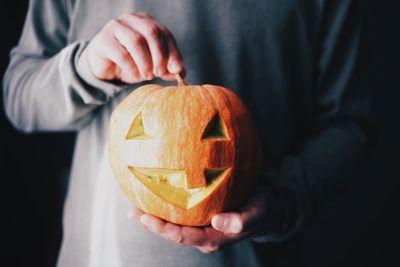 Midsection of person holding pumpkin against orange background