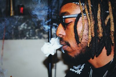 Side view of young man with dreadlocks smoking cigarette