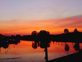 Silhouette trees by lake against sky during sunset