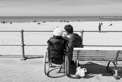 Rear view of people sitting on beach against sky